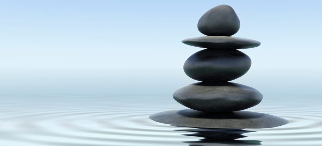 A stack of smooth stones balanced vertically in water, creating ripples around the base, against a foggy background, symbolizing that work-life balance is dead.