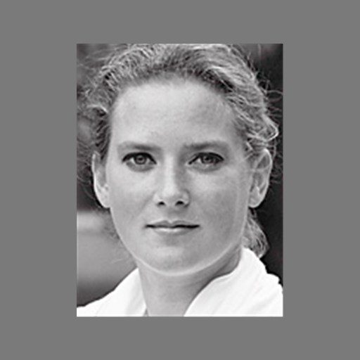 Black and white portrait of a woman with light-colored hair pulled back, looking directly at the camera, with a neutral expression, set against a plain gray background.