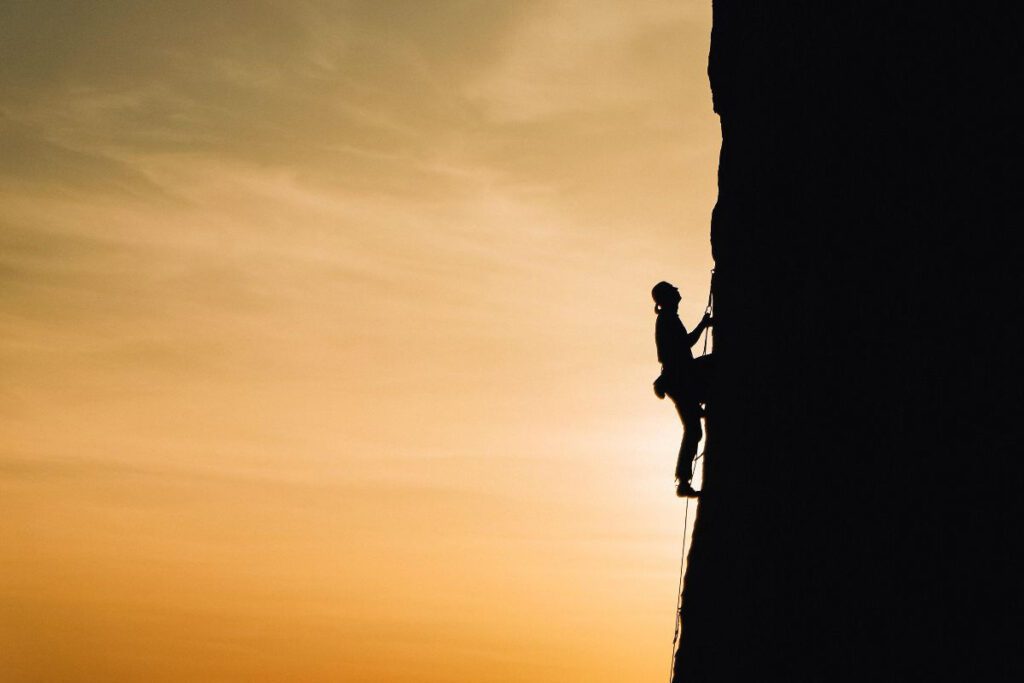 Silhouette of a climber ascending a steep cliff against a sunset sky, facing numerous CX challenges.